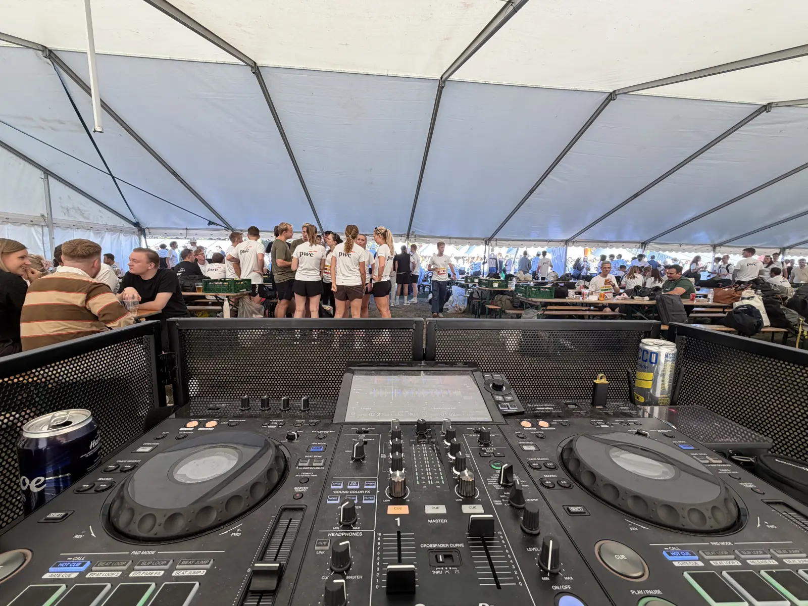 Set fra DJ-pulten ud over festteltet i Fælledparken: gæster i hvide løbetrøjer står i grupper og sidder ved langborde.