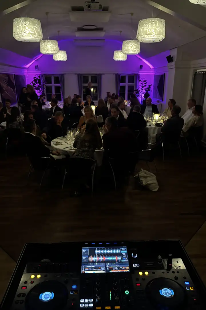 Gæster ved runde borde i en sal med stoflamper i loftet og lilla lys på væggene